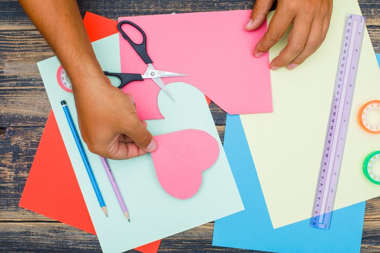 Foto gratuito concepto de artesanía con tijeras, regla, cintas, lápices sobre fondo de madera plana. hombre poniendo papel cortado a un lado.