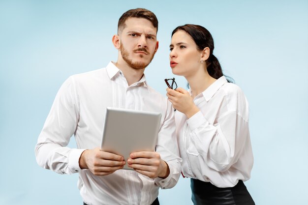 Concepto de asociación empresarial. Hombre y mujer joven mirando sospechoso contra el fondo azul en el estudio