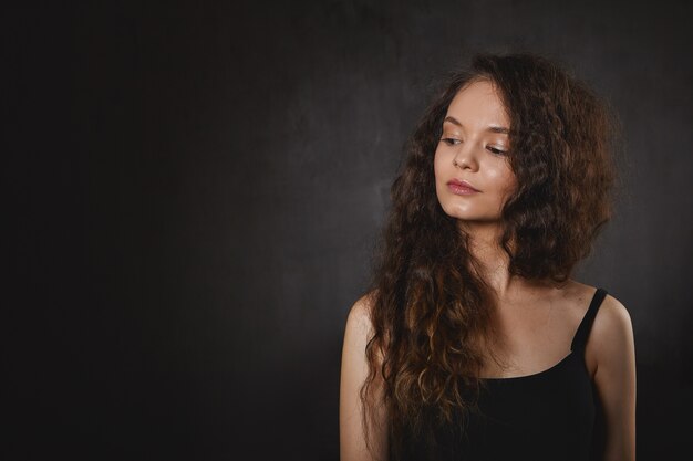 Concepto de astrología y misticismo. Hermosa mujer joven con cabello largo voluminoso mirando hacia abajo y sonriendo misteriosamente