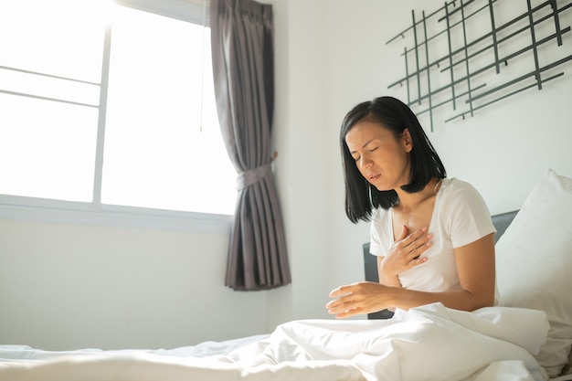 Foto gratuita concepto de ataque al corazón, la mujer asiática no puede trabajar, hoy está tan cansada. ella está enferma de un ataque de frecuencia cardíaca alta grave y aguda en la cama. mujer joven en pijama con ataque al corazón en su dormitorio.