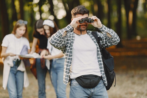 Concepto de aventura, caminata y personas. Grupo de amigos sonrientes en un bosque. Hombre con binoculares.