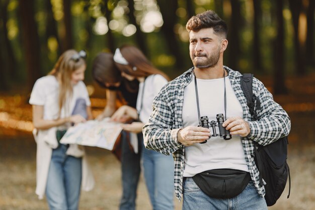 Concepto de aventura, caminata y personas. Grupo de amigos sonrientes en un bosque. Hombre con binoculares.