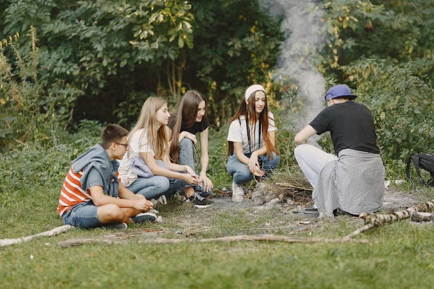 Concepto de aventura, viajes, turismo, caminata y personas. Grupo de amigos sonrientes en un bosque. Gente sentada cerca de la hoguera.