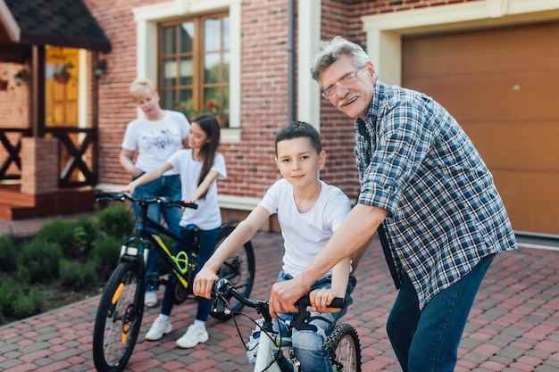 Concepto de ayuda, generación, seguridad y personas: abuelo feliz y niño con bicicleta y bicicleta enseñan juntos.