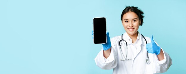 Foto gratuita concepto de ayuda en línea de atención médica web sonriente doctora o enfermera asiática que muestra la pantalla del teléfono inteligente ap
