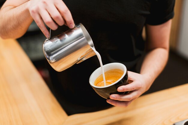 Concepto de bar con barista poniendo leche en café