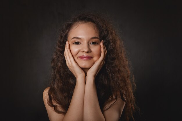 Concepto de belleza, alegría y felicidad. Retrato de encantadora mujer joven adorable descansando la barbilla sobre sus manos