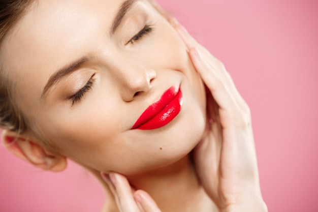 Concepto de belleza - Close up Hermosa mujer Morena joven cara retrato. Modelo de belleza Chica con cejas brillantes, maquillaje perfecto, labios rojos, tocando su cara. Aislado sobre fondo de color rosa