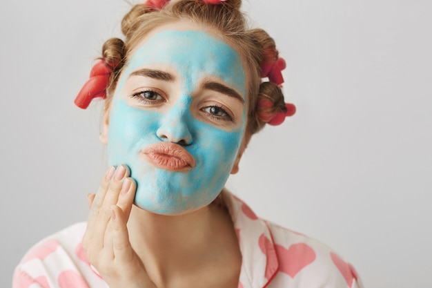 Concepto de belleza y cuidado de la piel. Chica en rizadores de pelo y ropa de dormir aplicar mascarilla facial