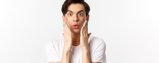 Concepto de belleza y lgbtq de personas Primer plano de hombre gay guapo expresa sorpresa mostrando las manos con esmalte de uñas azul de pie sobre fondo blanco