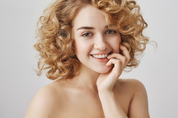 Concepto de belleza y moda. Despreocupada hermosa chica con cabello rizado y hombros desnudos sonriendo