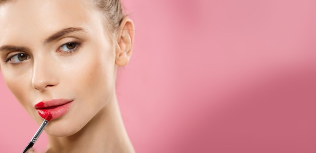 Concepto de belleza Mujer aplicando lápiz labial rojo con fondo de estudio rosa Hermosa chica hace maquillaje