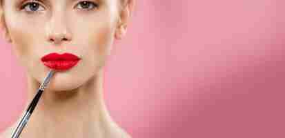 Foto gratuita concepto de belleza mujer aplicando lápiz labial rojo con fondo de estudio rosa hermosa chica hace maquillaje