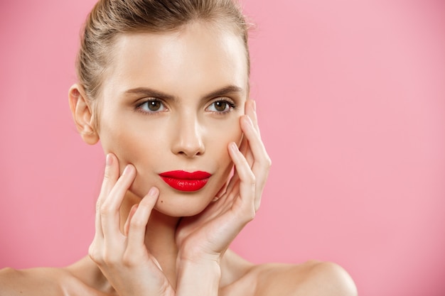 Concepto de belleza - mujer aplicar lápiz labial rojo con fondo de estudio de color rosa. Hermosa chica hace maquillaje.