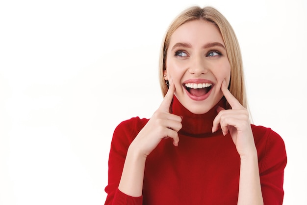 Concepto de belleza, mujeres y moda. Retrato de primer plano de tonta adorable joven rubia de cuello alto rojo