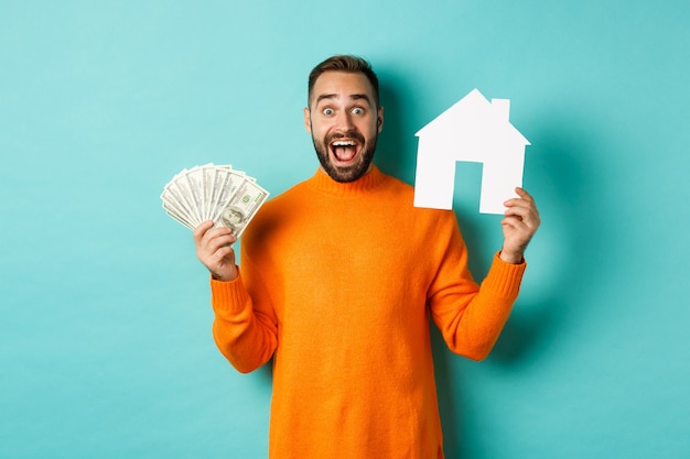 Concepto de bienes raíces y concepto de hipoteca. hombre emocionado mostrando dólares y maket de casa