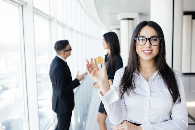 Concepto de blockchain e inversión. Líder de mujer de negocios sosteniendo bitcoin frente a discutir el equipo en la oficina.