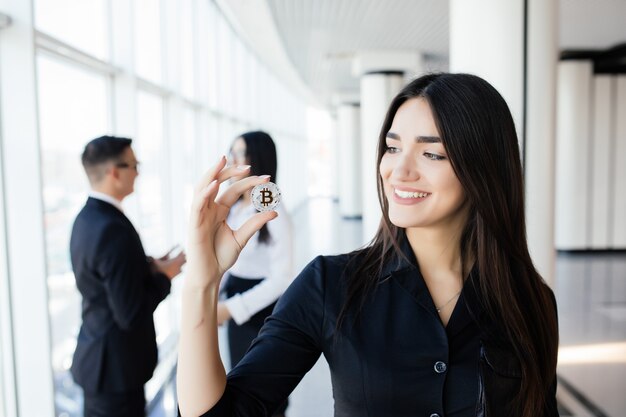 Concepto de blockchain e inversión. Líder de mujer de negocios sosteniendo bitcoin frente a su equipo de discusión en la oficina.