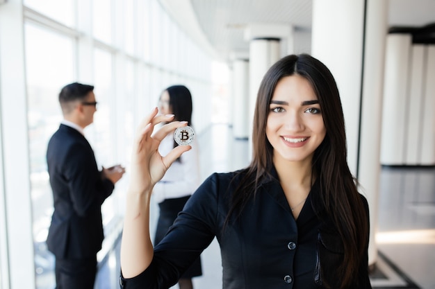 Concepto de blockchain e inversión. Líder de mujer de negocios sosteniendo bitcoin frente a su equipo de discusión en la oficina.