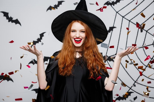 Concepto de bruja de Halloween: feliz y elegante bruja lanzando confeti para celebrar la fiesta de Halloween sobre la pared de murciélagos y arañas.