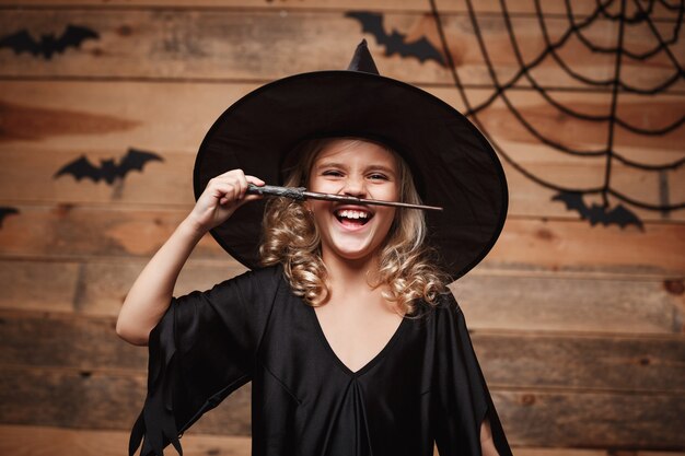 Concepto de bruja de Halloween - niño brujo disfruta jugando con varita mágica. sobre fondo de telaraña y murciélago.