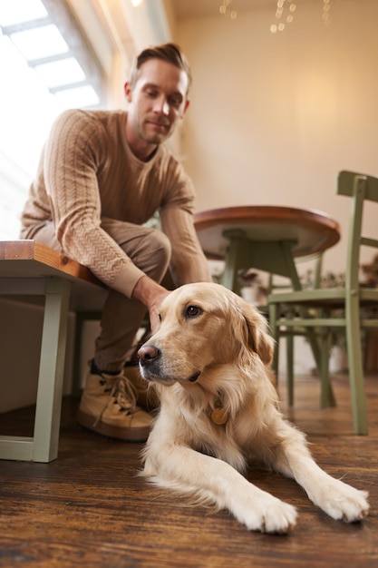 Un concepto de café amigable para perros hombre guapo dueño de un golden retriever se sienta en un café con sus bebidas para mascotas