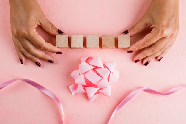 Concepto de celebración con arco, cinta en mesa rosa plana lay. Mujer sosteniendo cubos de madera.