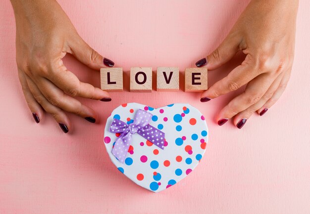 Concepto de celebración con caja de regalo en mesa rosa plana lay. Mujer sosteniendo cubos de madera.