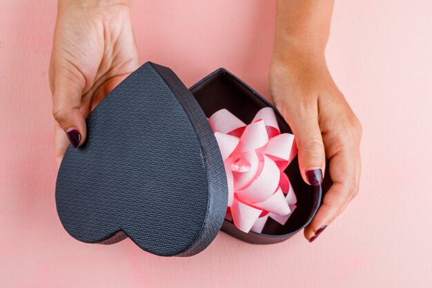 Concepto de celebración en mesa rosa plana lay. Mujer abriendo la caja de regalo.