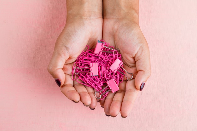 Concepto de celebración en mesa rosa plana lay. Mujer sosteniendo clips de papel y carpeta.