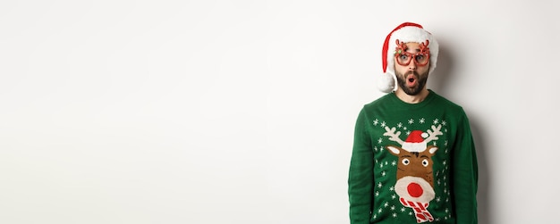 Foto gratuita el concepto de celebración navideña sorprendió al hombre con sombrero de santa y gafas de fiesta mirando algo