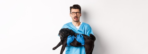 Concepto de clínica veterinaria veterinario triste sosteniendo perro pug negro y llorando sollozando con cara miserable sta