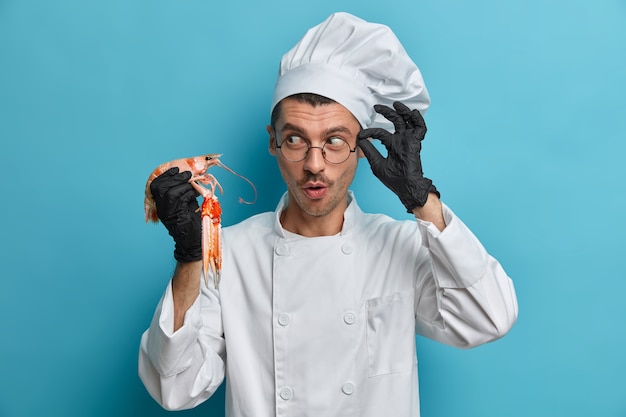 Concepto de cocina y mariscos. El chef profesional sostiene langostas o cangrejos de río crudos, prepara un plato vegetariano para ocasiones especiales, viste uniforme blanco