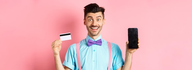 Foto gratuita concepto de comercio electrónico y compras hombre feliz que muestra la pantalla del teléfono inteligente vacía y la tarjeta de crédito de plástico rec