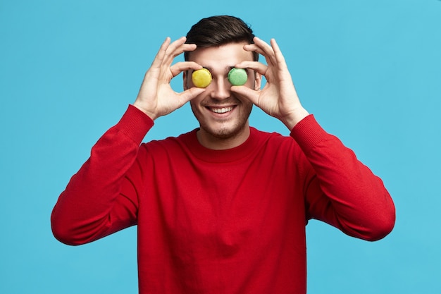 Concepto de comida, pastelería, alegría y diversión. Imagen de divertido joven sin afeitar macho en sudadera roja