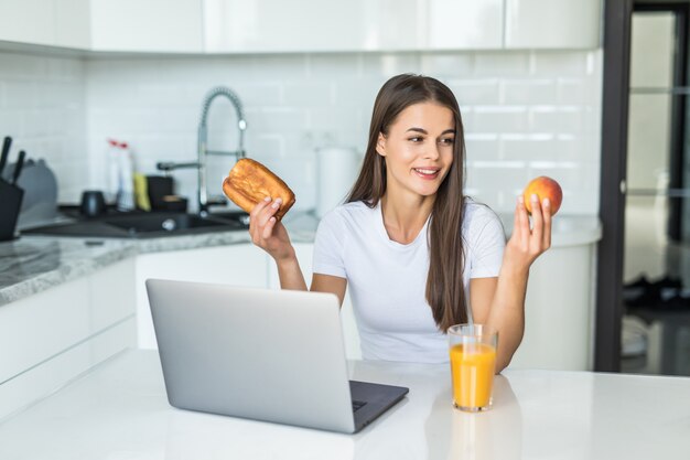 Concepto de comida saludable. Decisión difícil. La mujer deportiva de Yound está eligiendo entre alimentos saludables y dulces mientras está de pie en la cocina ligera.