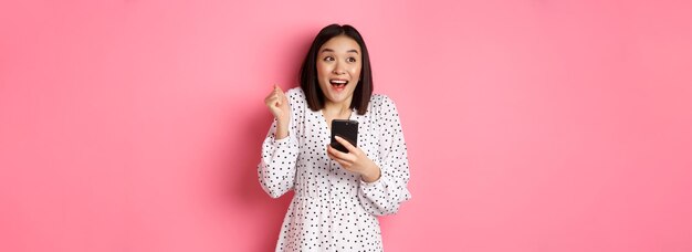 El concepto de compras y belleza en línea emocionó a la mujer asiática ganando en internet con teléfono inteligente y re