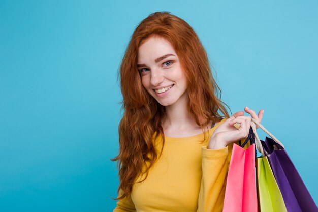 Concepto de Compras - Close up Retrato joven hermosa atractiva redhair niña sonriente mirando a cámara con bolsa de la compra. Fondo De Pastel Azul. Copie el espacio.