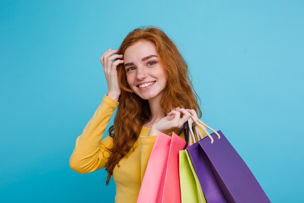 Concepto de Compras - Close up Retrato joven hermosa atractiva redhair niña sonriente mirando a cámara con bolsa de la compra. Fondo De Pastel Azul. Copie el espacio.