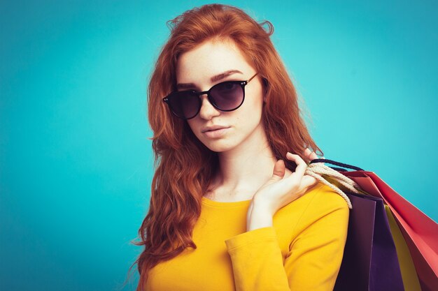 Concepto de Compras - Close up Retrato joven hermosa atractiva redhair niña sonriente mirando a cámara con bolsa de la compra. Fondo De Pastel Azul. Copie el espacio.