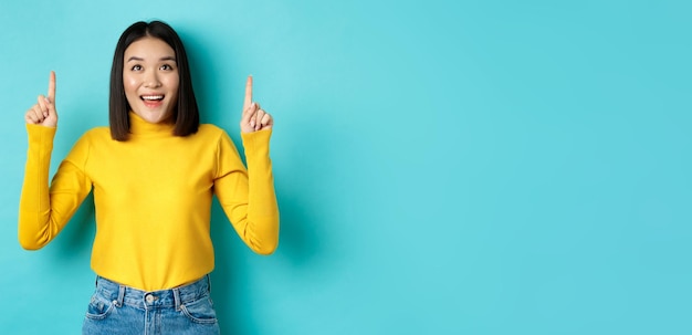 Foto gratuita concepto de compras hermosa mujer asiática en suéter amarillo apuntando con el dedo hacia el logo mirando el baile de graduación