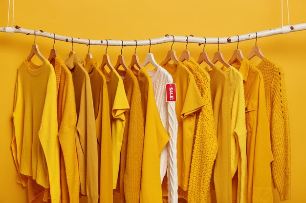 Concepto de compras y ofertas especiales. Muchos artículos de ropa amarilla y suéter de punto blanco con venta de etiqueta roja.
