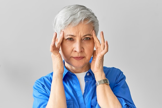 Foto gratuita concepto de concentración, pensamientos e ideas. creativa empresaria madura experimentada cogidos de la mano en las sienes, tratando de recordar algo. mujer mayor sufre de dolor de cabeza, con mirada dolorosa