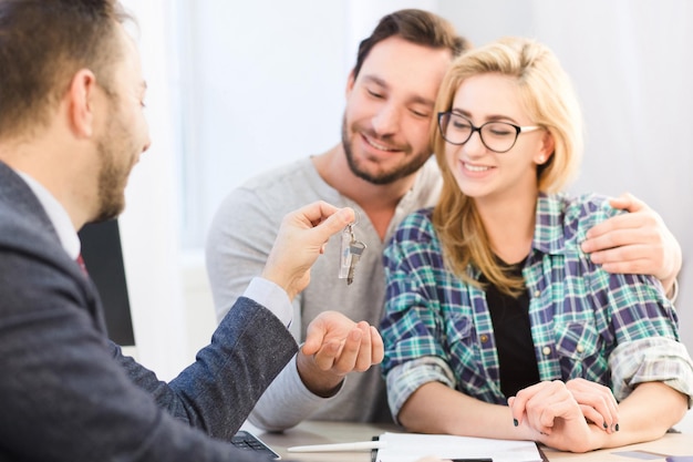 Concepto de concesionario. Concepto de banco. Tono de gerente de ventas dispuesto a entregar llave a joven pareja enamorada luego de firmar acuerdo o contrato de compra o venta.