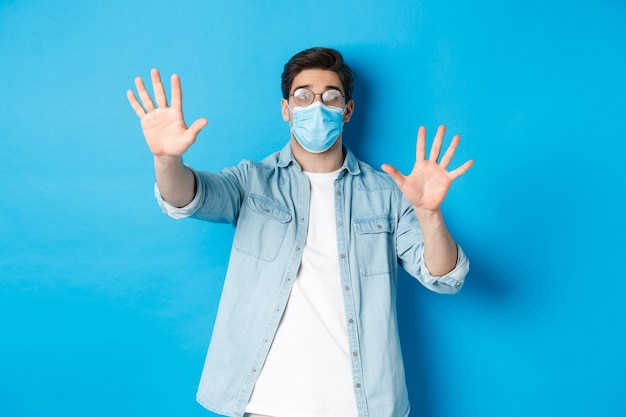 Concepto de coronavirus, distanciamiento social y pandemia. El hombre de cristal médico no puede ver en gafas de niebla, de pie sobre fondo azul.
