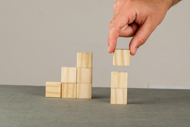 Concepto de crecimiento empresarial en vista lateral de la pared gris y blanco. Hombre arreglando bloque de madera apilando escalera.