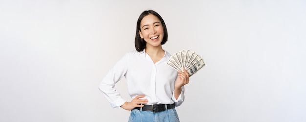 Concepto de crédito y préstamo sonriente joven asiática sosteniendo dólares en efectivo y mirando feliz a la cámara w