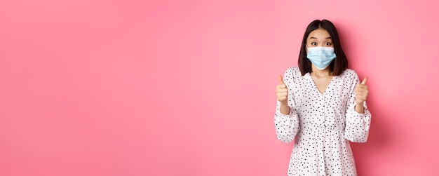 Foto gratuita el concepto de cuarentena y estilo de vida de covid emocionó a la mujer asiática con mascarilla mostrando el pulgar hacia arriba alabando ir