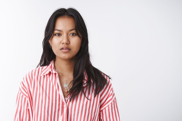 Concepto de cuerpo positivo, belleza y ternura. Atractiva joven vietnamita en blusa de rayas mirando suave y tiernamente a la cámara con la boca entreabierta, posando sobre fondo blanco