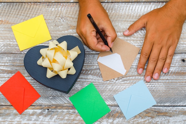 Concepto de cumpleaños con caja de regalo, sobres sobre fondo plano de madera endecha. Hombre escribiendo tarjetas de felicitación con lápiz.